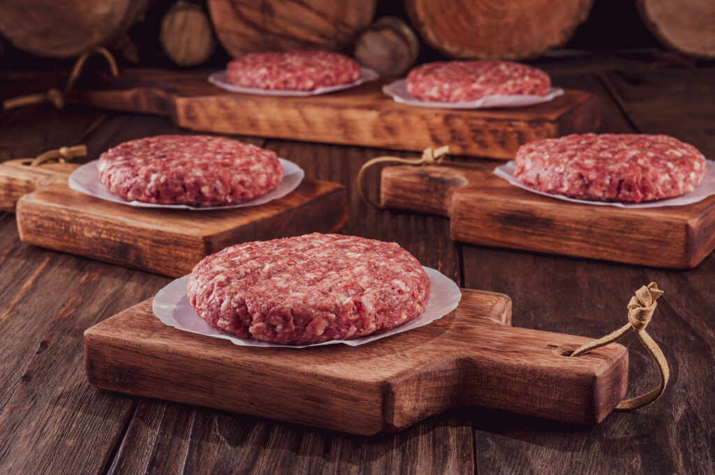 Raw,Hamburgers,On,Cutting,Board,With,Wood,Pile,Background